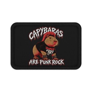 Puede incluir: Un parche rectangular negro con un capibara bordado con cresta roja, vistiendo una camiseta negra con el texto RANCID y una pulsera de pinchos. El texto CAPYBARAS ARE PUNK ROCK está bordado en blanco con contornos rojos arriba y abajo.