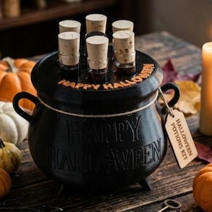 May include: A black cauldron with the text HAPPY HALLOWEEN embossed on the side and lid, containing six small glass vials with cork stoppers. A wooden tag attached to the handle reads HALLOWEEN POTIONS KIT. The cauldron is surrounded by pumpkins.
