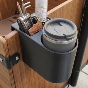 Könnte beinhalten: Ein schwarzer Kunststoff-Getränkehalter an einer hölzernen Lastenradbox. Der Halter enthält einen grauen Reisebecher mit Deckel, einen Satz silberner Metall-Inbusschlüssel, eine kleine durchsichtige Röhre mit einer Karte und einen braunen Lederanhänger.