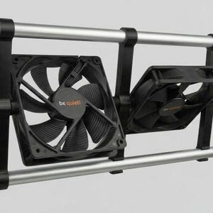 May include: Two black square computer cooling fans with the text be quiet! printed on the center, mounted on a horizontal frame consisting of two parallel silver metal rods connected by black plastic brackets, attached to two vertical green poles.