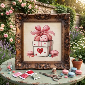 May include: A framed cross-stitch embroidery depicting a white gift box filled with pink macarons, topped with a large pink bow and the word love written in red. The ornate brown frame features heart motifs, accompanied by embroidery floss, scissors, and a thimble.