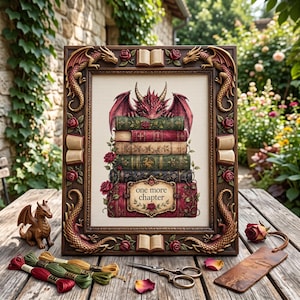 May include: A framed cross-stitch embroidery featuring a red dragon perched atop a stack of books with the text one more chapter. The dark brown frame is decorated with sculpted dragons, open books, and red roses, with embroidery floss nearby.