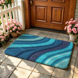 May include: A rectangular floor mat featuring a wavy, abstract pattern in shades of deep navy, royal blue, and bright turquoise. The mat has a textured, tufted surface and is positioned on a stone patio in front of a wooden door and white fence.