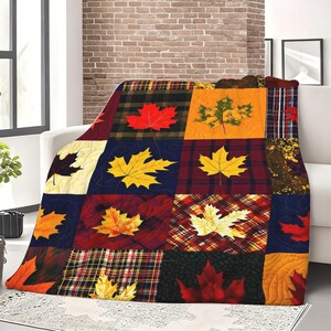 May include: A plush throw blanket featuring a patchwork design of various autumn-themed squares. The pattern includes alternating blocks of plaid, solid colors, and textured fabrics, each decorated with vibrant maple leaf motifs in red, orange, and yellow.