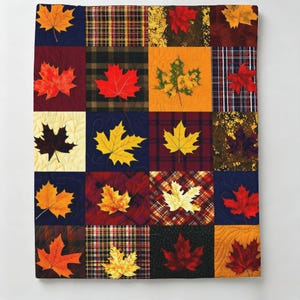 May include: A patchwork quilt featuring a grid of squares with alternating patterns of autumn maple leaves and various plaid or textured fabrics in shades of red, orange, yellow, brown, and navy blue, finished with visible machine quilting stitches.