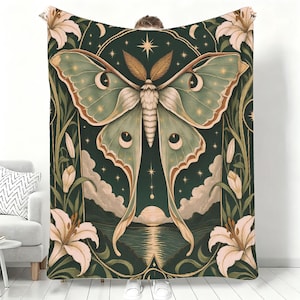May include: A dark green throw blanket featuring a large central moth with pale green wings, surrounded by white lily flowers, stars, and a crescent moon. The design includes a landscape with a rising sun over water at the bottom.