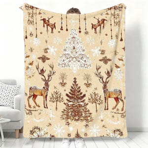 May include: A beige fleece blanket featuring a repeating pattern of brown deer, white Christmas trees, and white snowflakes. The design includes hanging ornaments and small tree illustrations scattered across the fabric in a symmetrical layout.