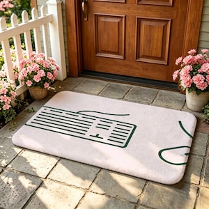 May include: A rectangular light-colored floor mat featuring a dark green graphic print of a computer keyboard and a computer mouse. The mat has a soft, textured surface and is positioned on a stone patio in front of a wooden door.