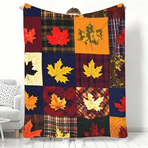 May include: A quilted throw blanket featuring a patchwork design of various autumn-themed squares. The pattern includes alternating blocks of solid colors, plaid, and checkered fabrics, each decorated with vibrant red, yellow, and orange maple leaves.