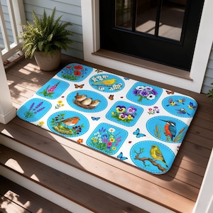 Puede incluir: Un felpudo rectangular con fondo blanco y múltiples paneles con bordes azules. Los paneles muestran ilustraciones coloridas de varias aves, incluyendo petirrojos y martines pescadores, junto con arreglos florales, mariposas e insectos.