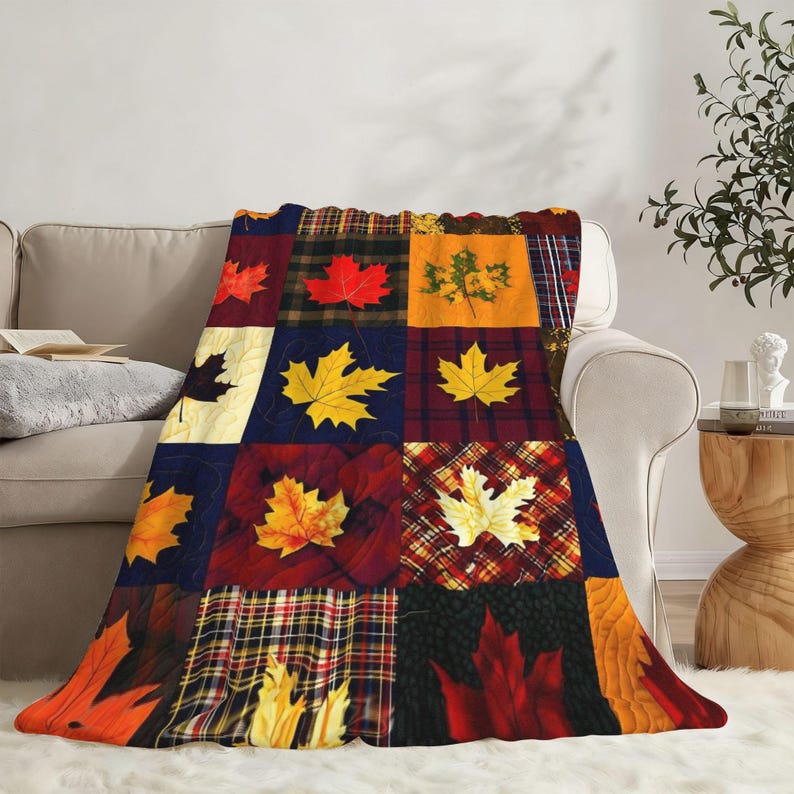 May include: A soft throw blanket featuring a patchwork design of various autumn maple leaves in shades of red, orange, yellow, and brown. The pattern includes alternating squares of solid colors, plaid, and textured backgrounds with maple leaf motifs.