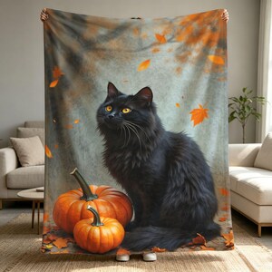 Puede incluir: Una manta rectangular que muestra un gato negro de pelo largo sentado junto a dos calabazas naranjas. El fondo presenta una textura gris suave y tenue con hojas de otoño naranjas dispersas por toda la escena.