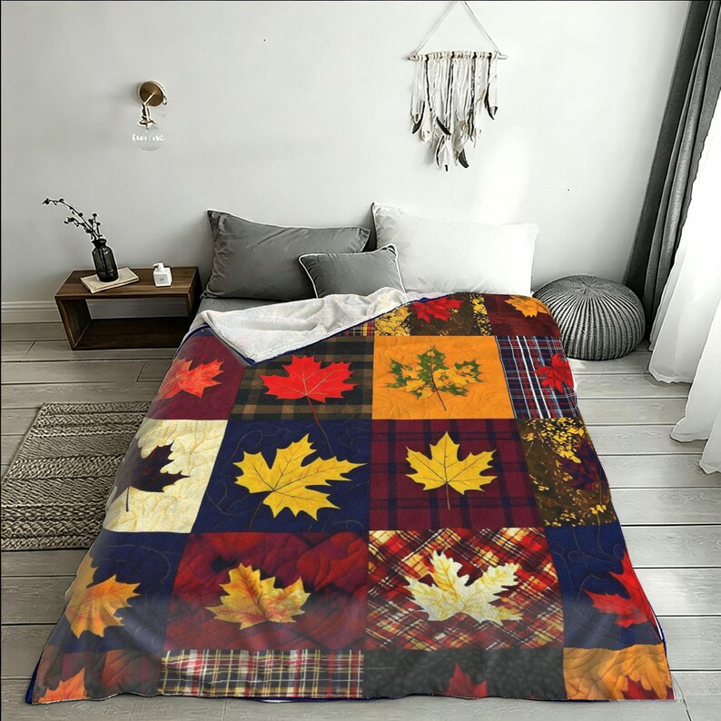 May include: A rectangular quilt featuring a patchwork design of various autumn-themed squares. Each square displays different patterns including plaid, tartan, and solid colors, decorated with printed maple leaves in shades of red, yellow, and orange.