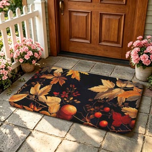 May include: A rectangular doormat featuring a black background with a printed pattern of autumn leaves in shades of orange, yellow, and brown, interspersed with small red berries and round orange fruits, creating a seasonal botanical design.