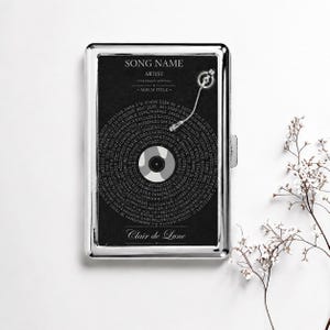 May include: A rectangular silver metal case featuring a black graphic design of a vinyl record with a tonearm. The text reads SONG NAME, ARTIST, YOUR MESSAGE (OPTIONAL), ALBUM TITLE, and Clair de Lune. The record surface contains small text.