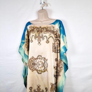 May include: A long, flowing, cream-colored kaftan with a blue and white tie-dye pattern on the sleeves. The kaftan features a gold and brown ornate pattern throughout.