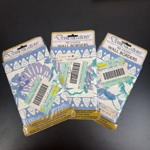 May include: Three pre-pasted wall border rolls with a blue, white, and purple floral design. Each roll is labeled "Domestications" and includes a barcode and text. The borders are packaged in clear plastic.