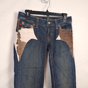 May include: Dark blue denim jeans with a white and brown patchwork design. The jeans have a low rise and a straight leg.