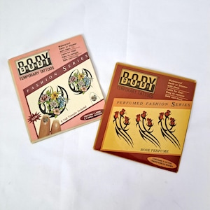 May include: Two packages of Body Druz temporary tattoos. One is pink with floral designs and nail transfers. The other is brown with rose designs. Both packages are labeled "Perfumed Fashion Series" and "Fashion Series."