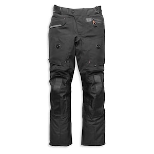 May include: Black motorcycle trousers featuring a reinforced waistband with a button closure, zipped pockets with orange pull tabs, integrated circular ventilation ports on the thighs, and textured knee panels for added durability and protection.