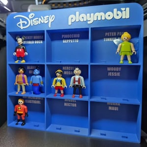 Pode incluir: Uma prateleira de exibição azul de plástico Playmobil Disney com nove compartimentos. A prateleira apresenta etiquetas de texto branco para os nomes dos personagens. Sete pequenas figuras de plástico estão colocadas nas ranhuras, incluindo Mickey Mouse, Aladdin, Genie, Pinocchio, Hercules, Mr. Incredible e Tinker Bell.