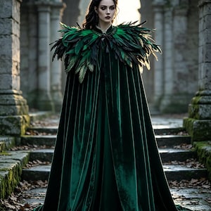 May include: A floor-length dark green velvet cloak featuring a high collar adorned with layered black and green feathers. The garment drapes to the floor with a smooth, heavy texture and is fastened at the neck with a dark, ornate clasp detail.