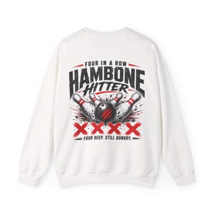 May include: A white long-sleeve sweatshirt featuring a graphic on the back with the text "FOUR IN A ROW HAMBONE HITTER" above a bowling ball striking pins, with four red X symbols below and the text "FOUR DEEP. STILL HUNGRY." at the bottom.