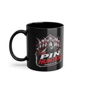 Könnte beinhalten: Eine schwarze Keramiktasse mit einer Grafik einer Bowlingkugel, die Pins in einem roten Fadenkreuz trifft. Der Text PIN HUNTER und LOCKED ON THE PINS ist in Weiß und Rot gedruckt. Das Design enthält Bewegungslinien und Trümmer.