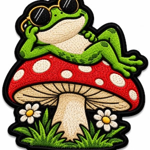 Puede incluir: Un parche bordado que muestra una rana verde con gafas de sol de montura amarilla, recostada sobre una seta roja grande con puntos blancos. La seta está rodeada de hierba verde y dos pequeñas margaritas blancas con centro amarillo sobre un borde negro.