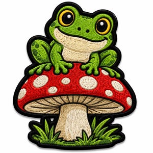 Puede incluir: Un parche bordado que muestra una rana de color verde brillante con grandes ojos amarillos sentada sobre una seta roja con puntos blancos. La seta tiene un tallo beige y está rodeada de briznas de hierba verde, todo con un borde negro.