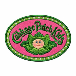 Puede incluir: Un parche bordado ovalado con el texto verde Cabbage Patch Kids arqueado sobre una ilustración central de una cara sonriente dentro de hojas de col verdes, sobre un fondo rosa con un borde verde y puntos blancos.