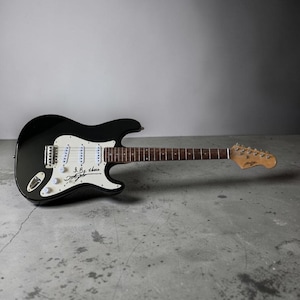 May include: A black electric guitar with a white pickguard, three white single-coil pickups, and a wooden fretboard. The white pickguard features a black handwritten signature and the phrase I'll Be There written in black ink on the body.