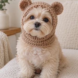 May include: A light brown crochet pet hat featuring two small rounded bear ears on top. The hat is designed to fit snugly around the head and neck, with a textured knit pattern and a wide opening for the face, providing a warm and cozy appearance.