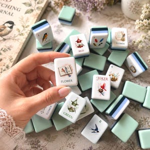 May include: A collection of rectangular mahjong tiles featuring pastel mint green backs and white faces with colorful illustrations of birds, birdhouses, nests, and floral motifs. Each tile displays specific text labels like Flower, Red, Green, Joker, and numbers.