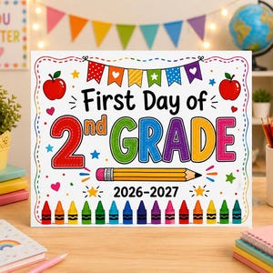 Könnte beinhalten: Ein rechteckiges weißes Schild mit dem Text First Day of 2nd GRADE 2026-2027. Das Design zeigt bunte Illustrationen einer Wimpelkette, zwei rote Äpfel, einen gelben Bleistift und eine Reihe bunter Wachsmalstifte am unteren Rand des Schildes.