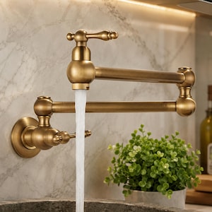 May include: A wall-mounted pot filler faucet with a brushed brass finish, featuring a double-jointed swing arm and a single lever handle. A steady stream of water flows from the aerator, which is positioned over a dark stone basin.