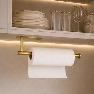 May include: A brushed gold metal paper towel holder mounted under a cabinet shelf. The holder features a horizontal rod with a circular end cap, supporting a roll of white paper towels with a textured pattern. The finish is matte and metallic.