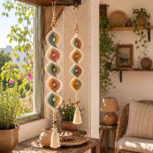 Può includere: Due decorazioni verticali da appendere con un design a uncinetto a spirale in tonalità tenui di verde salvia, rosa antico, giallo senape e crema. Ogni pezzo è sospeso da un cordino con perline di legno e rifinito con una nappa in filato crema.