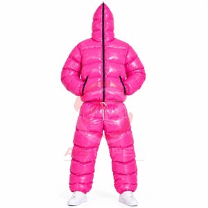 Puede incluir: Un mono acolchado de color rosa brillante con un acabado de alto brillo, que cuenta con una cremallera frontal completa que sube hasta la capucha integrada. La prenda tiene un diseño aislante con cámaras horizontales en chaqueta y pantalón.