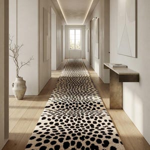 Peut inclure: Un long tapis de couloir présentant une base de couleur crème avec un motif répétitif de taches noires irrégulières. Le tapis est placé au centre sur un plancher en bois clair dans un couloir, s'étendant du premier plan vers une fenêtre lointaine.