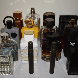 Puede incluir: Una colección de frascos de perfume variados de diferentes formas, tamaños y colores, incluyendo recipientes de vidrio transparente, negro, blanco y amarillo. Algunos frascos tienen tapas metálicas, mientras otros tienen superficies oscuras.