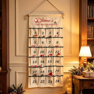 Pode incluir: Um calendário de contagem decrescente de Natal em tecido creme para pendurar na parede, com vinte e quatro bolsos numerados a verde. O topo apresenta o texto Jenna's CHRISTMAS COUNTDOWN com um gráfico do Pai Natal e uma corda.