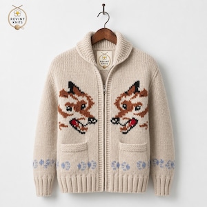 May include: A beige knit zip-up cardigan featuring a shawl collar and two front pockets. The garment displays two brown and black fox face motifs on the chest and a pattern of small blue paw prints along the bottom hem. A Revint Knits label is inside.