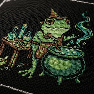 May include: A cross-stitch embroidery on black fabric featuring a green frog wearing a pointed hat and apron. The frog stands beside a wooden table with glass vials and a mortar and pestle, stirring a steaming green liquid in a large cauldron.