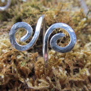 May include: A silver hammered metal ring with a double spiral design. The ring is made of a thick gauge wire and has a rustic, handmade look.