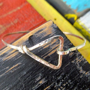 May include: A silver hammered triangle bangle bracelet with a simple, minimalist design. The bracelet is open and has a hammered finish.