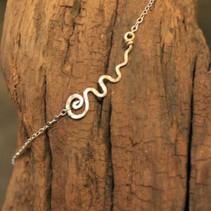 May include: A silver chain necklace with a wavy, abstract design pendant. The pendant is made of hammered silver and has a spiral shape at one end. The chain has a small gold bead.