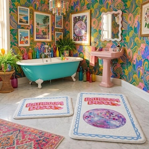 Puede incluir: Dos alfombrillas de baño rectangulares blancas con un borde festoneado azul y el texto "BATHROOM DISCO" en letras rosas. La alfombrilla más grande incluye un gráfico de una bola de discoteca, mientras que la pequeña tiene un corazón rosa.