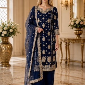 May include: A deep navy blue salwar kameez set featuring intricate gold embroidery throughout the tunic and wide-leg trousers. The ensemble includes a matching sheer navy blue dupatta with a wide gold embroidered border along the edges.