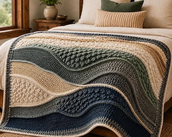 Op de afbeelding: Een rechthoekige gehaakte deken met golvende, horizontale kleurstroken in crème, beige, saliegroen en donker marineblauw. Het ontwerp bevat diverse gestructureerde steken, waaronder noppen en dichte rijen, wat zorgt voor een gelaagd effect.